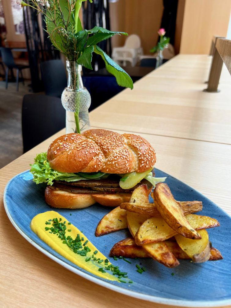 Ein Burger mit Kartoffelspalten und Senf auf einem blauen Teller auf einem Tisch im Life Deli im Jüdischen Museum