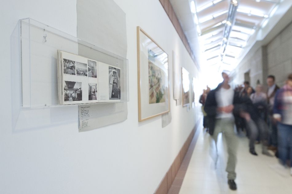 Gruppe von Menschen (verschwommen, rechts) im Gang des Architekturmuseums, links Fotos an der Wand