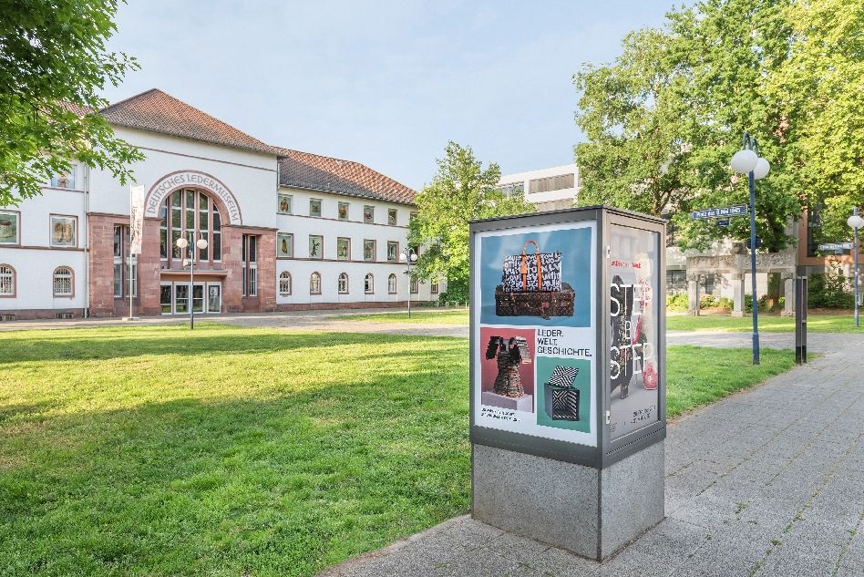 Blick auf den Eingang des Ledermuseums im Hintergrund mit eckiger Plakatsäule im Vordergrund