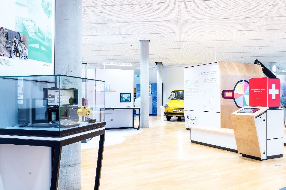 Dauerausstellung des Museums für Kommunikation mit Vitrine im Vordergrund links und gelben Postauto im Hintergrund