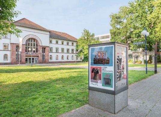 Blick auf den Eingang des Ledermuseums im Hintergrund mit eckiger Plakatsäule im Vordergrund