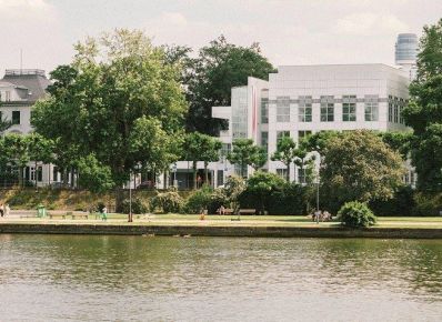 Museumsufer Frankfurt mit Museum Angewandte Kunst und Villa Metzler im Vordergrund der Fluss, einige Passanten am Ufer mit Bäumen, im Hintergrund die Museumsgebäude