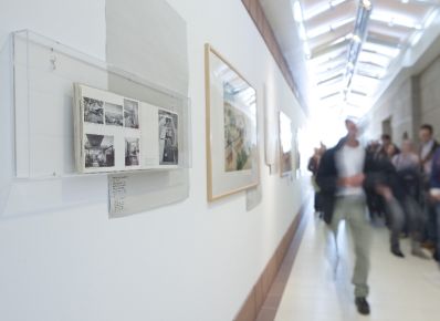 Gruppe von Menschen (verschwommen, rechts) im Gang des Architekturmuseums, links Fotos an der Wand