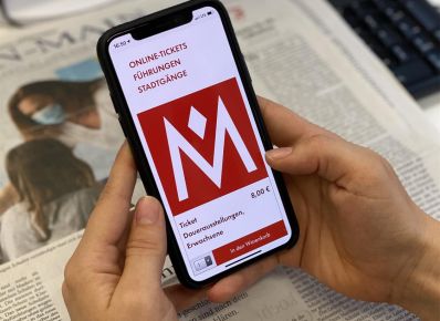 Eine Person hält ein Handy in der Hand, auf dem Display die responsive Ansicht des Museumsshop des Historischen Museums