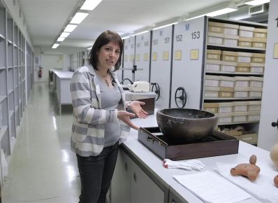 Die Kuratorin Dr. Natascha Bagherpour steht vor einer Theke mit einer großen Schale im Lager des Archäologischen Museums