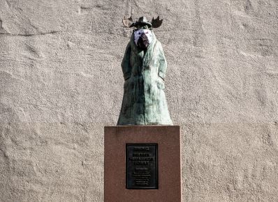 Statue von einem stehenden Elch im Mantel mit Maske vor dem Caricatura Museum